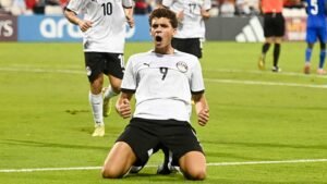 Egyptian striker celebrates on the pitch, kneeling with arms raised in triumph, during a significant match in international competition.