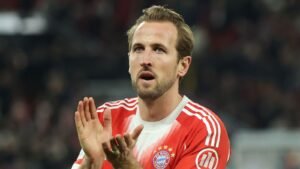 Harry Kane, gekleed in het rode tenue van Bayern München, klapt enthousiast en toont vastberadenheid in een stadionsfeer.