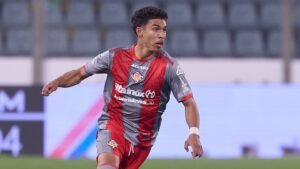 Un joueur de football marocain, en tenue grise et rouge, sprinte sur le terrain, illustrant l'intensité d'un match compétitif.