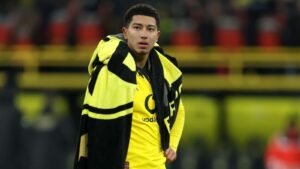 جوب بيلينغهام، مرتديًا زي بوروسيا دورتموند الأسود والأصفر، يقف ملفوفًا ببطانية تحمل شعار النادي على أرضية الملعب.