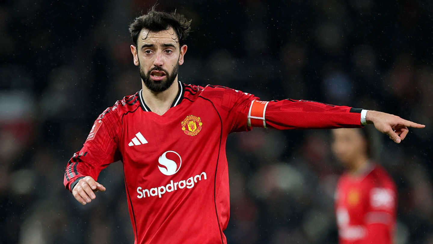 Bruno Fernandes in Manchester United's red kit, gesturing during a match, highlighting his leadership on the pitch amid a rainy backdrop.