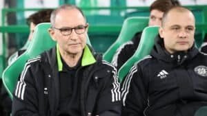 Martin O’Neill et son assistant sont assis sur le banc du Celtic, vêtus de vestes d’entraînement noires à bandes blanches, dans un stade de couleur verte.