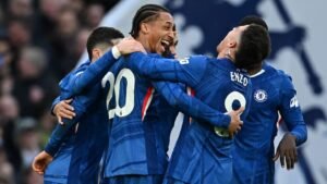 Chelsea players in vibrant blue kits celebrate joyfully after a goal, showcasing teamwork and excitement in a packed stadium.