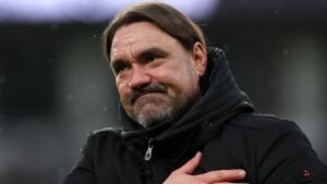 Daniel Farke toont een pijnlijke uitdrukking in een zwarte jas, reflecterend op een uitdagend moment voor zijn team tijdens een wedstrijd.