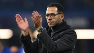 L'entraîneur, vêtu d'un élégant manteau noir et de lunettes, saluant la foule, illustrant un moment de reconnaissance envers l'équipe pendant un match.