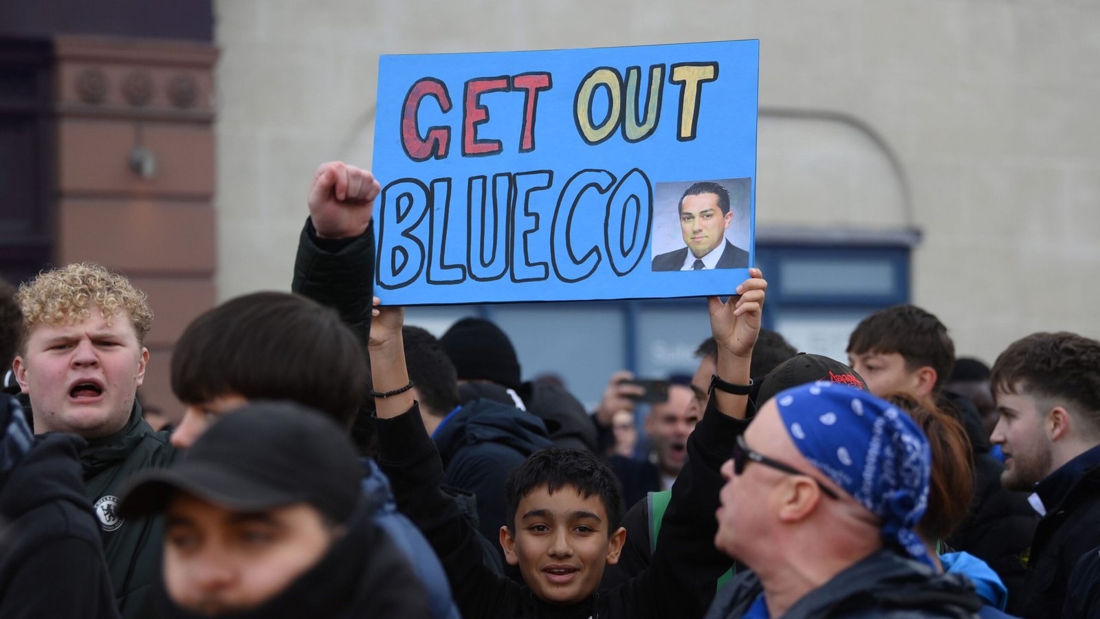 Les supporters de Chelsea manifestent à l'extérieur de Stamford Bridge, brandissant une pancarte bleue sur laquelle on peut lire "GET OUT BLUECO" accompagnée d'une photo, illustrant leur mécontentement.