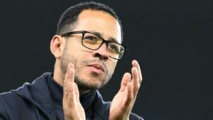 Liam Rosenior, dans une veste sombre et des lunettes, gesticule avec passion lors d'une discussion sur le football, soulignant son engagement dans le sport.