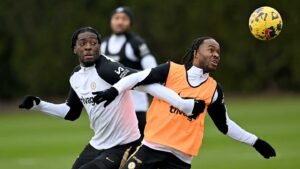 Chelsea players in training, featuring Raheem Sterling in an orange bib and a teammate in black, both focused on a football.