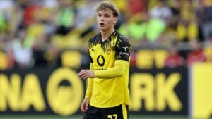 Cole Campbell, vêtu du maillot noir et jaune du Borussia Dortmund, apparaît concentré pendant un match, les supporters flous en arrière-plan.