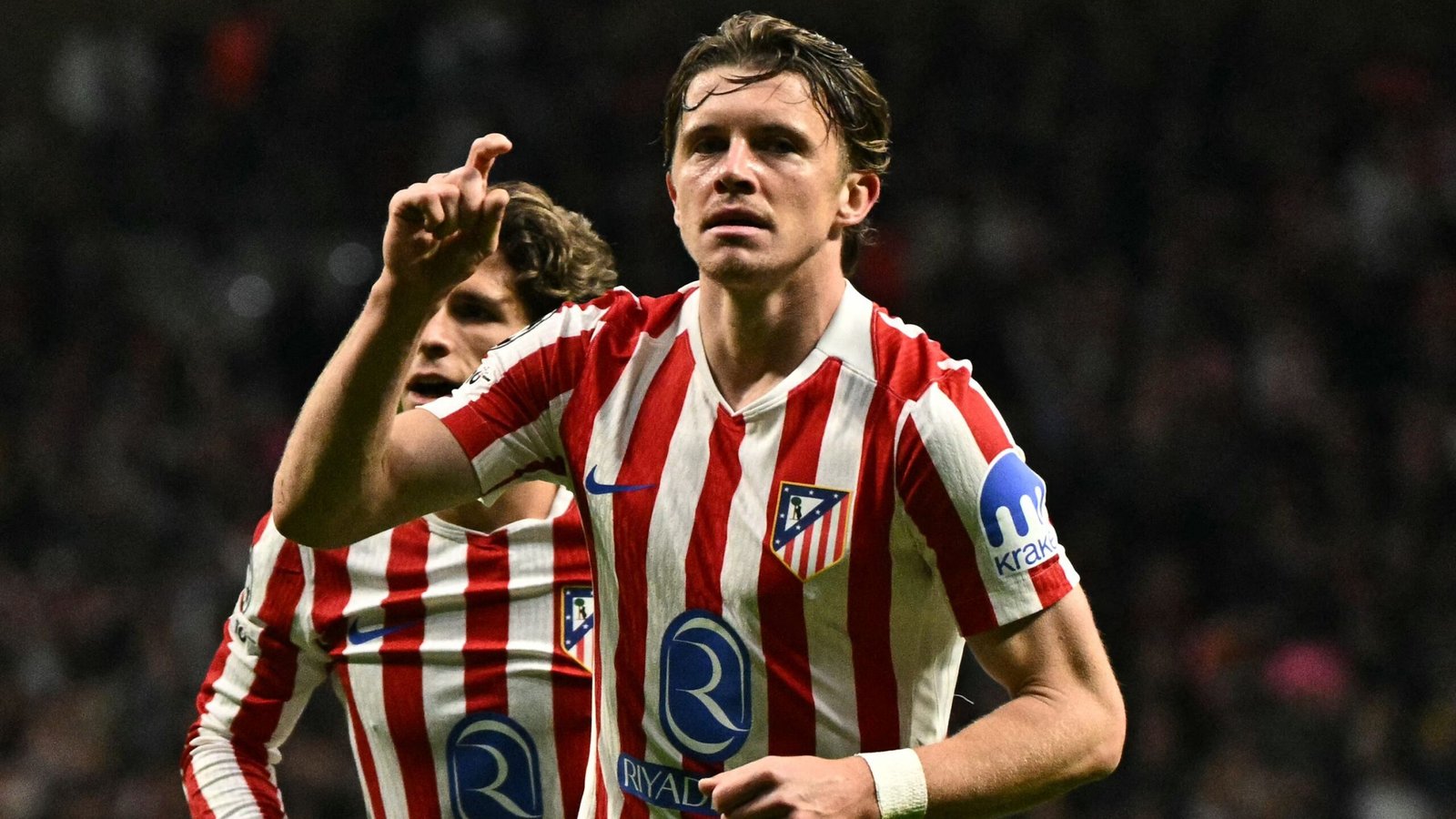 Conor Gallagher viert na een doelpunt voor Atlético Madrid, gekleed in het rood-wit gestreepte tenue van het team, met fans op de achtergrond.