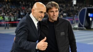 Conte en Spalletti delen een moment op het veld, waarbij Conte een duim omhoog steekt; beiden dragen formele kleding tegen de achtergrond van een stadion.