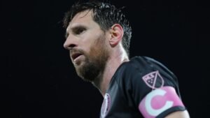 Lionel Messi in een zwart shirt met een roze aanvoerdersband, gefocuste uitdrukking, die zijn status in het voetbal benadrukt.