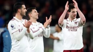 Les joueurs d'Arsenal célèbrent après un match, portant des tenues blanches avec des détails rouges, applaudissant les supporters dans le stade.