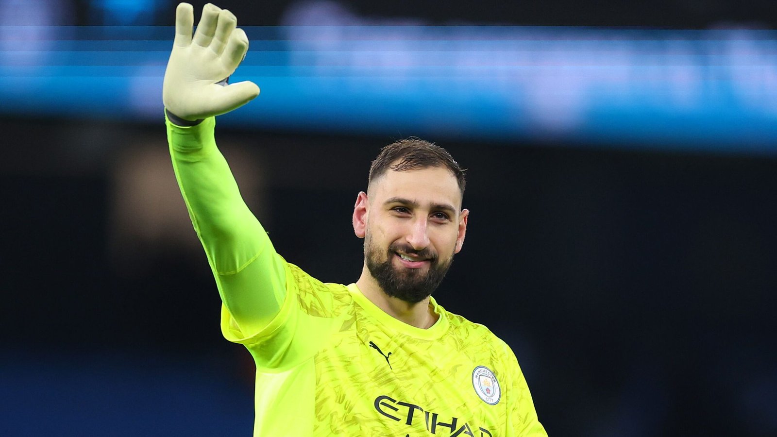 Donnarumma, dans un maillot vert vif de Manchester City, salue la foule avec un sourire, illustrant son rôle de gardien de but.