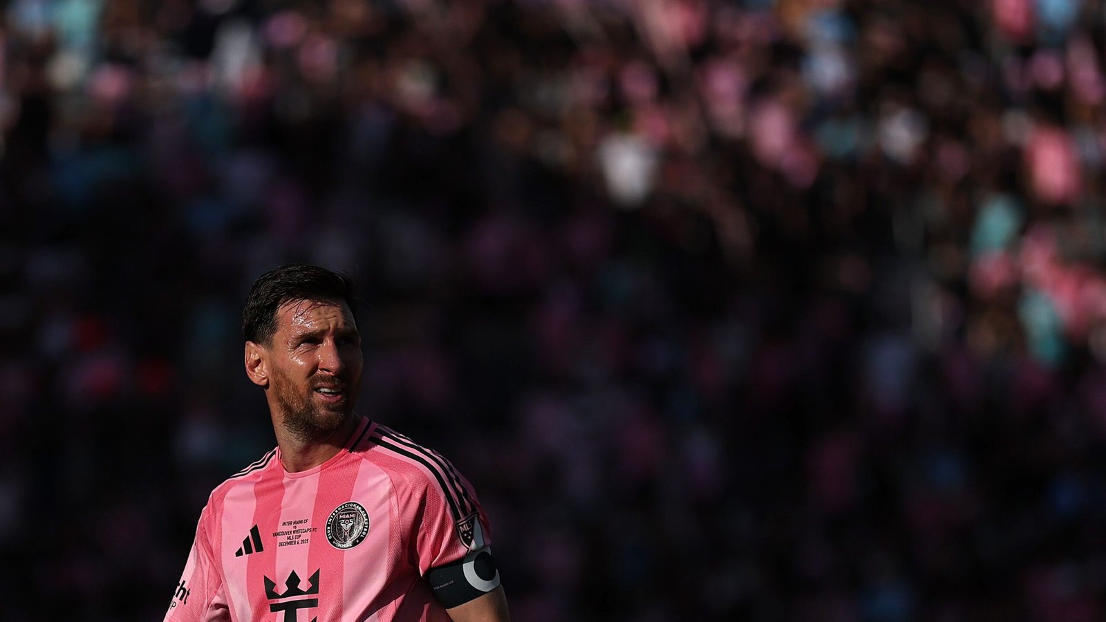 Lionel Messi, portant le maillot rose d'Inter Miami, regarde intensément tandis qu'une foule vibrante remplit l'arrière-plan pendant un match.