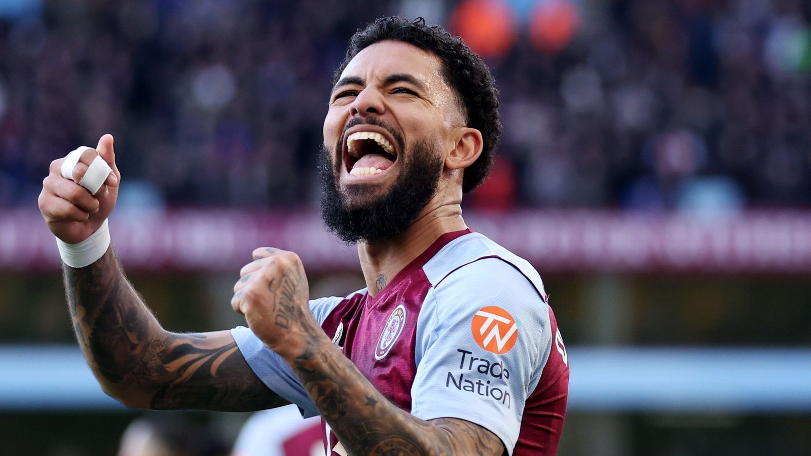Douglas Luiz celebrating passionately after a goal, wearing Aston Villa's claret and blue kit, showcasing intense emotion and determination.