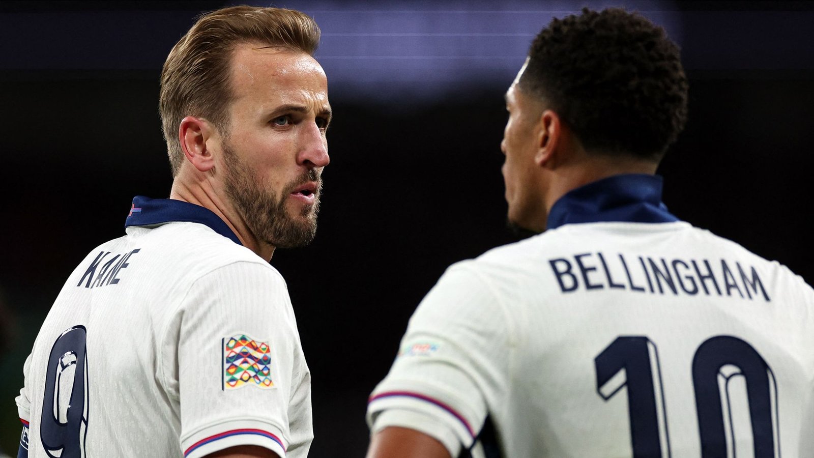 Harry Kane en Jude Bellingham in Engelse tenues, geconcentreerd op elkaar tijdens een wedstrijd, wat teamwork en intensiteit toont.