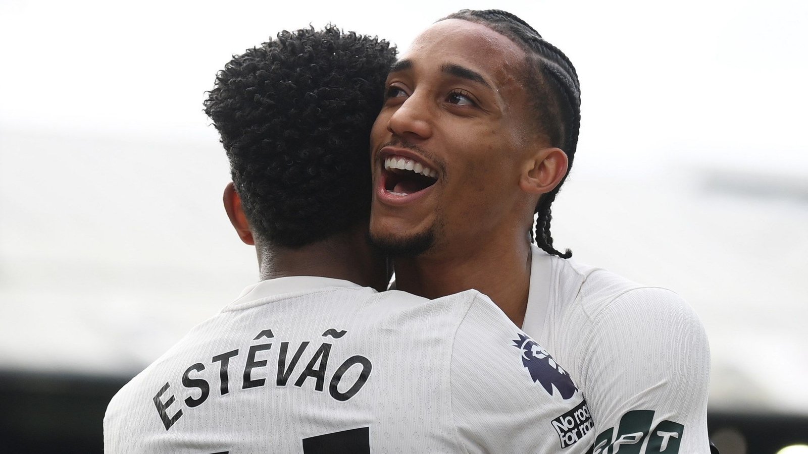 Estevão omarmt João Pedro tijdens het vieren, beiden in het witte tenue van Chelsea, en toont vreugde na een overwinning in de wedstrijd.