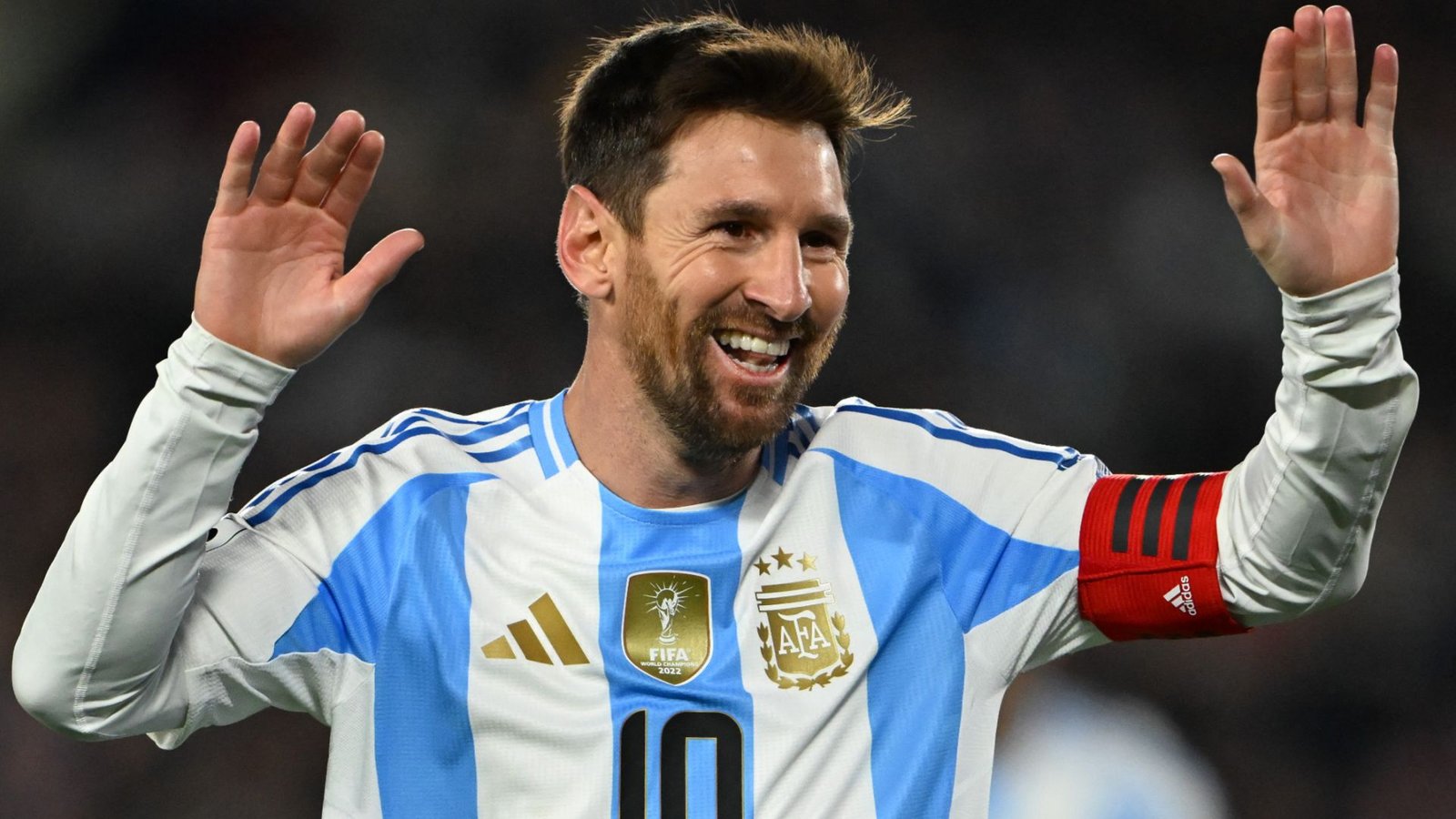 Lionel Messi, gekleed in het lichtblauw-witte tenue van Argentinië en met de aanvoerdersband, lacht en zwaait tijdens een wedstrijdviering.