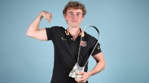 Young footballer in a black Barcelona polo flexes his bicep while holding a sleek silver trophy against a light blue backdrop.