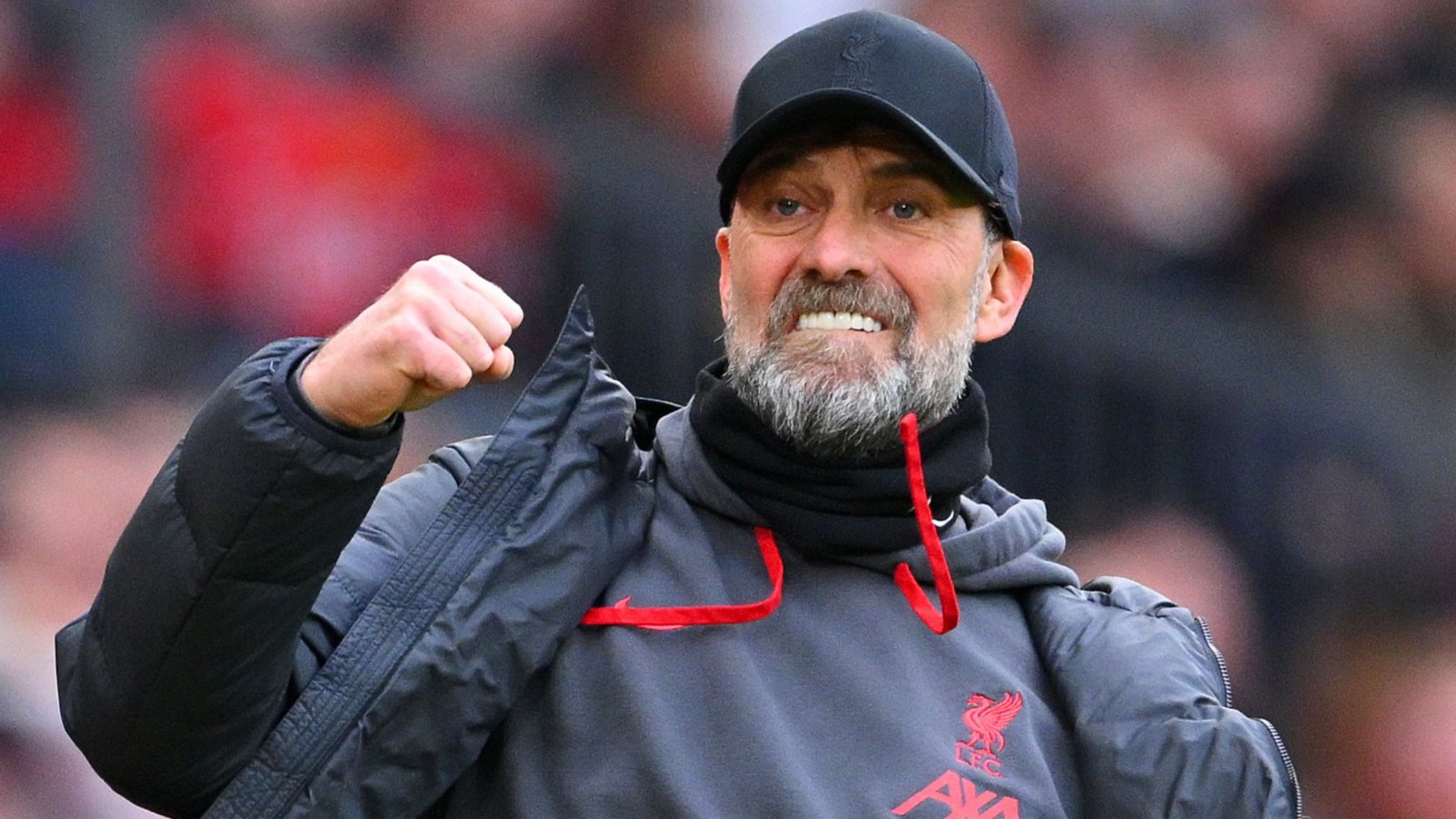Jurgen Klopp die gepassioneerd viert aan de zijlijn, gekleed in een Liverpool-pet en jas, te midden van een levendige stadionsfeer.