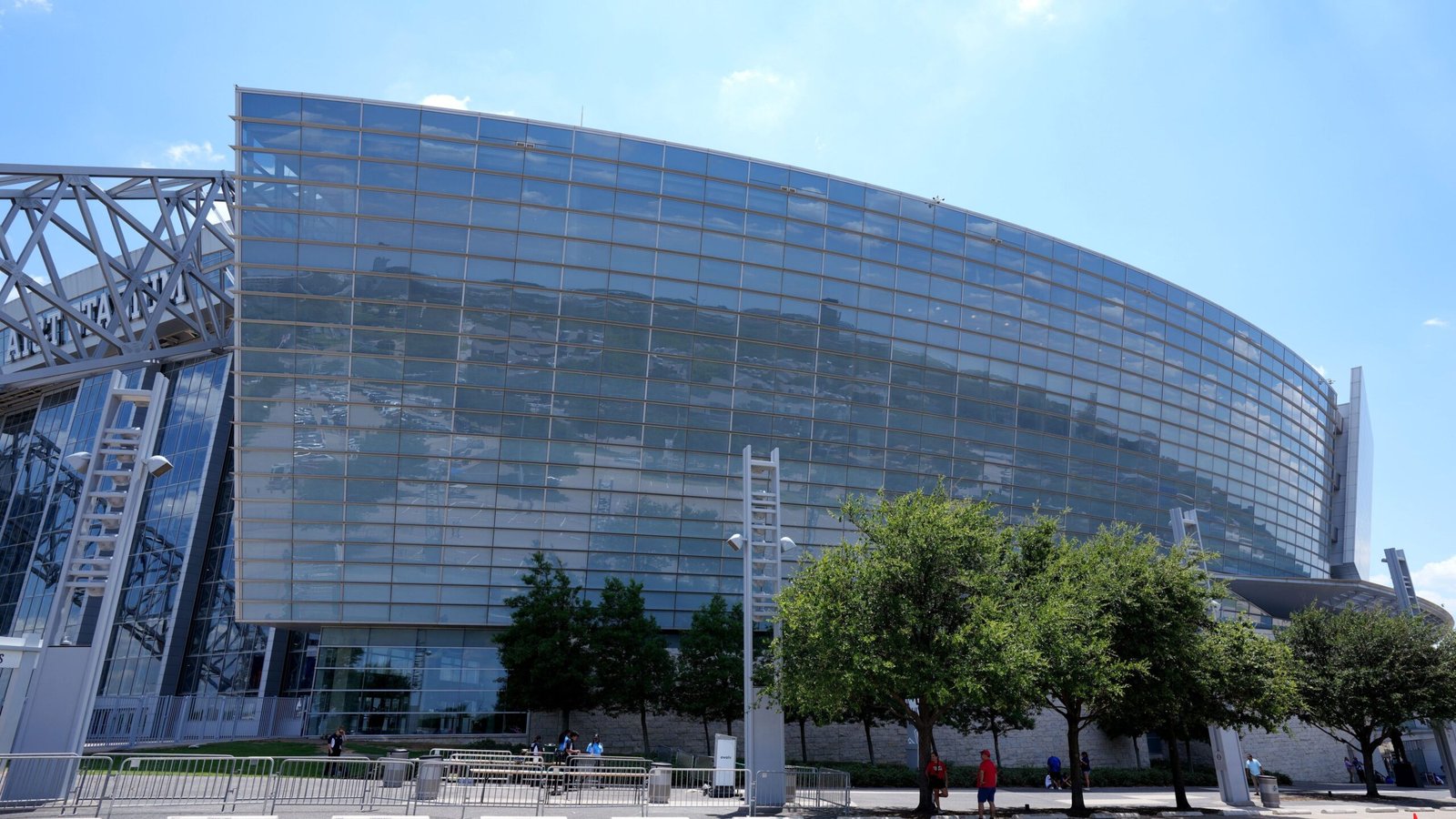 Geglazuurde gevel van een modern stadion onder blauwe hemel, omgeven door groen en supporters, ter illustratie van de infrastructuur voor het FIFA WK 2026.