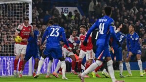 Arsenal's player holds the ball near the goal as Chelsea players contest the play, creating a tense moment in the match.