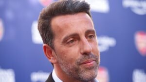 Edu Gaspar, ancien directeur d'Arsenal, est vu de profil contre un fond bleu avec des logos d'Arsenal, affichant une expression contemplative.