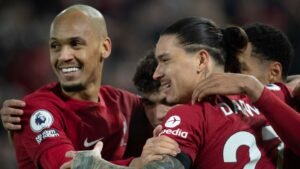 Fabinho et Darwin Núñez célèbrent un but pour Liverpool, portant leurs kits rouges emblématiques, dans un décor de coéquipiers jubilants.