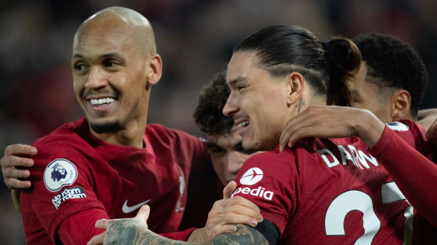 Fabinho et Darwin Núñez célèbrent un but pour Liverpool, portant leurs kits rouges emblématiques, dans un décor de coéquipiers jubilants.