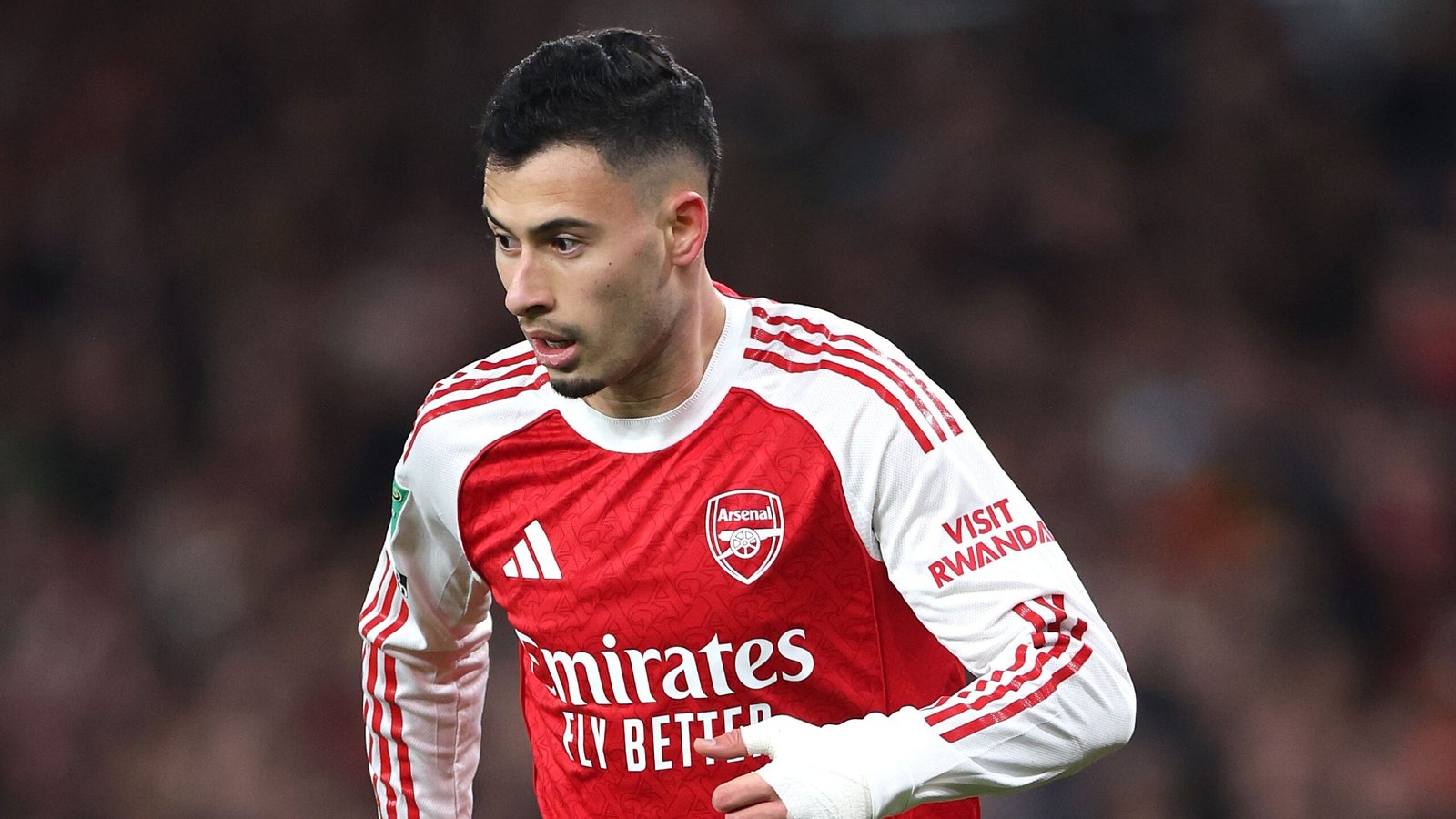 Gabriel Martinelli, in het opvallende rode tenue van Arsenal, jogt geconcentreerd over het veld tijdens een wedstrijd, waarbij de clubhuisstijl wordt getoond.