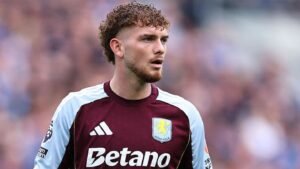 Harvey Elliott dans le maillot grenat et bleu ciel d'Aston Villa, concentré sur le jeu pendant un match, mettant en lumière sa détermination et son talent.