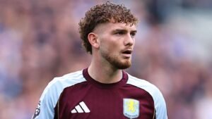 Harvey Elliott, in an Aston Villa kit, displays a focused expression during a match, showcasing his curly hair and team logo.