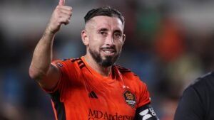 Hector Herrera célèbre dans le maillot orange vif du Houston Dynamo, souriant et faisant un signe de pouce levé pendant un match.