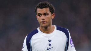 Dele Alli dans le maillot blanc et bleu marine de Tottenham Hotspur, l'air pensif pendant un match, un éclairage mettant en valeur son expression concentrée.