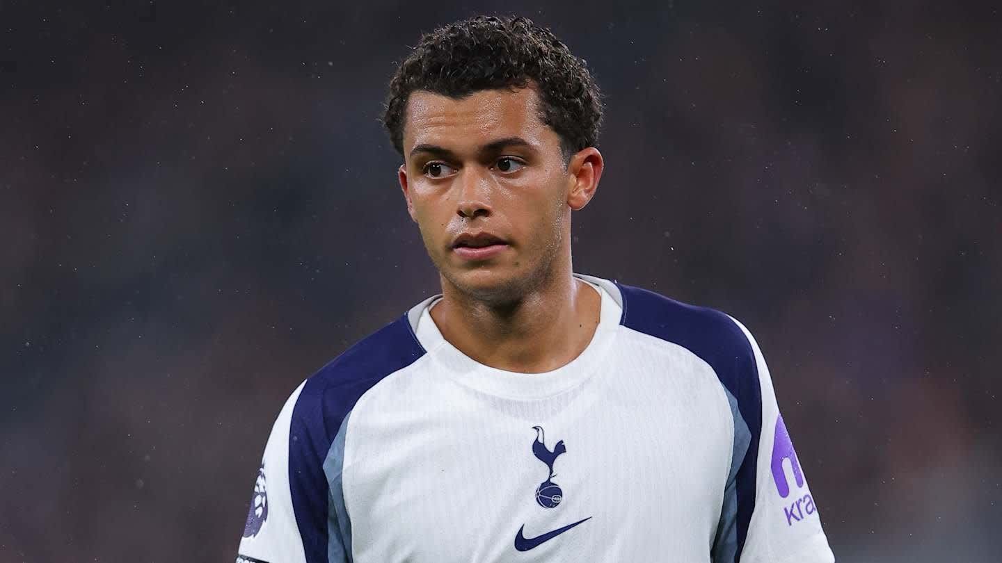 Dele Alli dans le maillot blanc et bleu marine de Tottenham Hotspur, l'air pensif pendant un match, un éclairage mettant en valeur son expression concentrée.