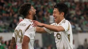 كوانغيو ومويا يحتفلان بفرح في الملعب، يرتديان زيًا أبيض مع لمسات ذهبية، وسط حشد مشجع.