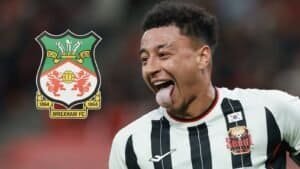 Jesse Lingard célèbre joyeusement dans un maillot à rayures noires et blanches, le logo de Wrexham FC étant clairement visible en arrière-plan.