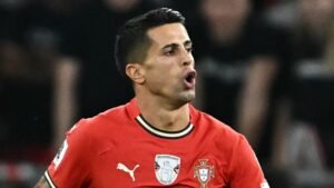 João Cancelo in een rood Portugal-tenue, gepassioneerd reagerend tijdens een UEFA Nations League-wedstrijd, met een geconcentreerde gezichtsuitdrukking.