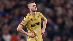 Adam Wharton, in een gouden Crystal Palace-tenue met "NET88"-logo, ziet er gefrustreerd uit op het veld tijdens een Premier League-wedstrijd.