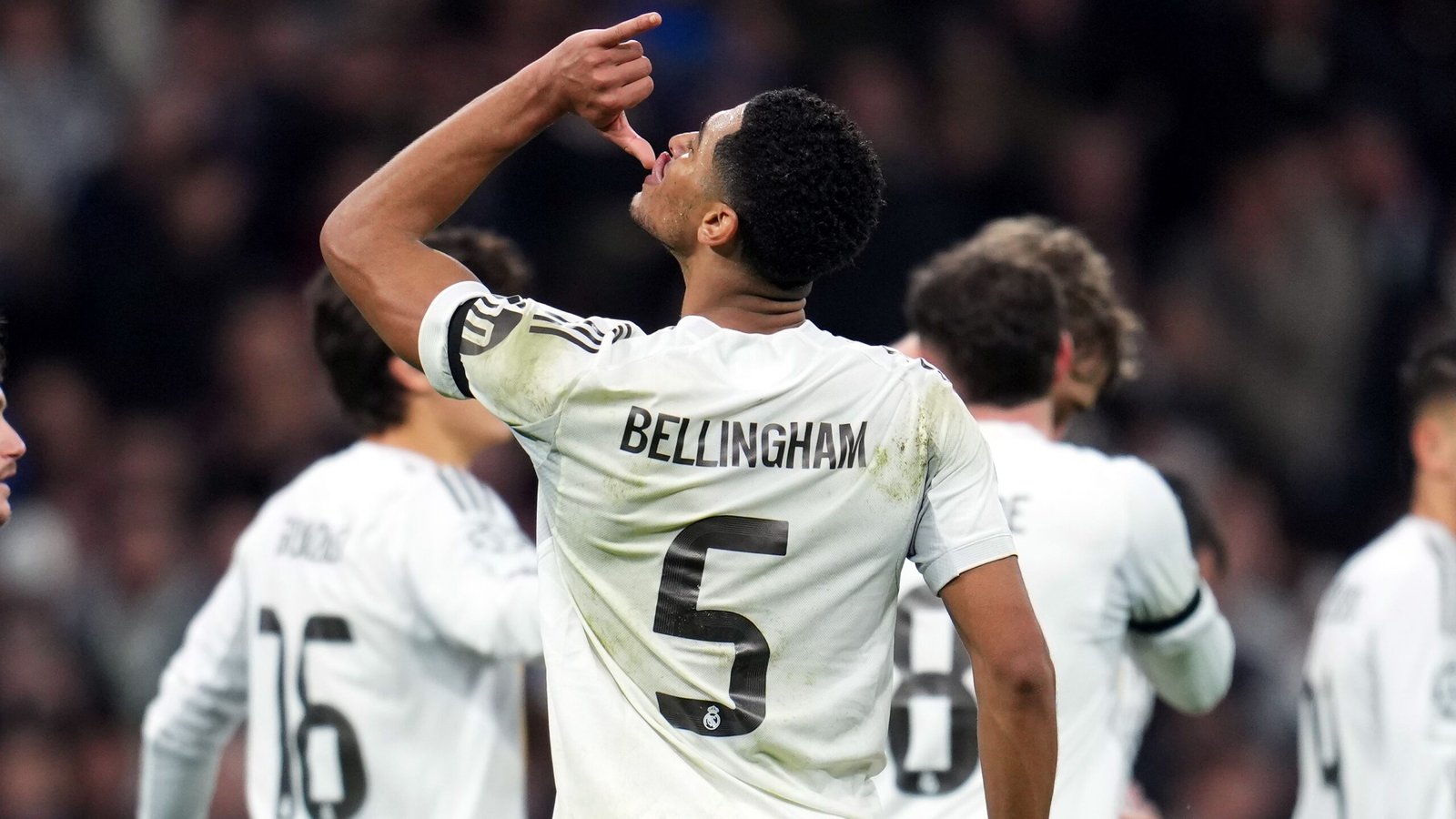 Jude Bellingham viert een doelpunt met een uniek drinkgebaar, gekleed in een Real Madrid-tenue, omringd door teamgenoten.