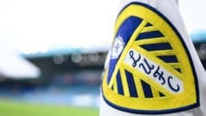 Het embleem van Leeds United is prominent weergegeven in blauw en geel, met een gestileerd ontwerp met ingewikkelde details.