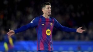 Robert Lewandowski, in a Barcelona kit featuring blue and claret, gestures expressively during a match, hinting at possible future moves.