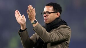 ليام روزينيو، يرتدي معطفاً بنياً ووشاحاً أسود، يصفق بحماس معبراً عن التشجيع خلال مباراة.