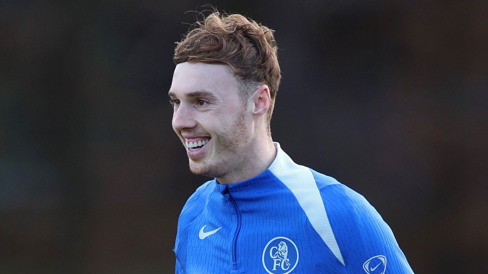 Cole Palmer smiles during a training session, wearing a blue Chelsea FC tracksuit with the club badge visible.