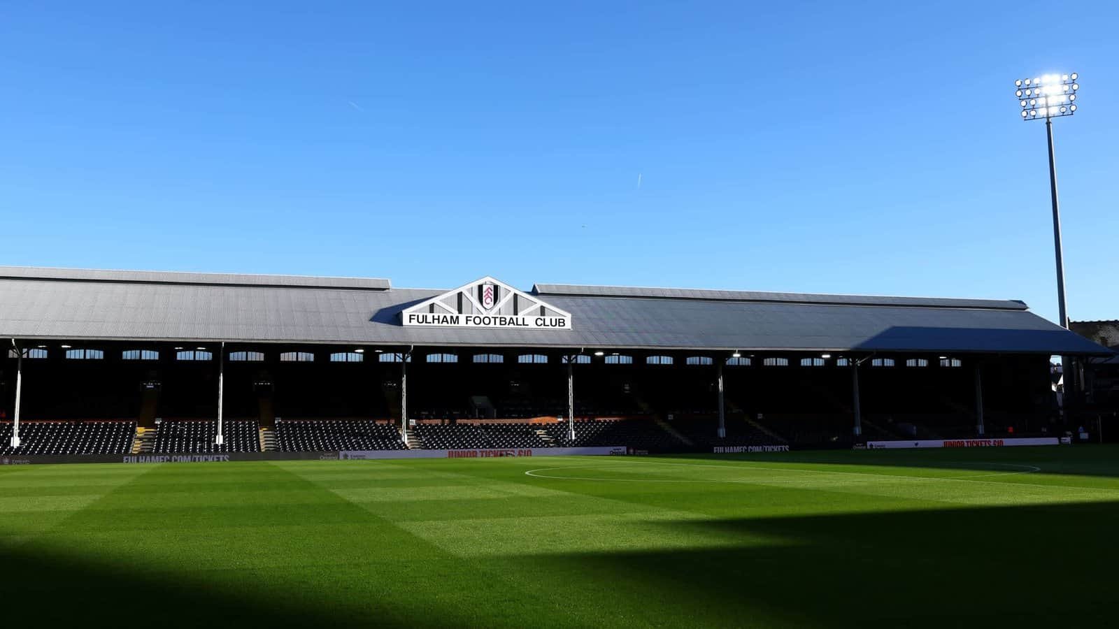 Le Craven Cottage de Fulham FC sous un ciel bleu dégagé, présentant un terrain vert impeccable et la tribune emblématique avant un match contre Liverpool.