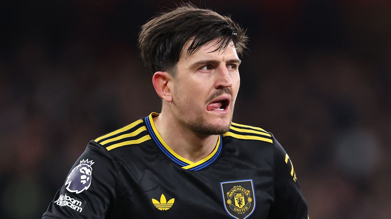 Harry Maguire in het zwarte tenue van Manchester United, toont intense concentratie en vastberadenheid tijdens een wedstrijd, met het Premier League-logo op zijn mouw.