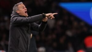 Luis Enrique gebaart gepassioneerd vanaf de zijlijn tijdens een PSG-wedstrijd, gekleed in een donkere jas tegen een wazige achtergrond van toeschouwers.