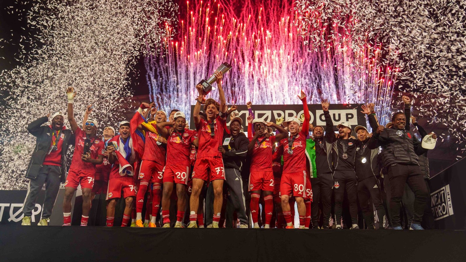 Des joueurs célébrant, vêtus de maillots rouges, soulèvent le trophée au milieu des confettis et des feux d'artifice lors de la cérémonie de la MLS Next Pro Cup.
