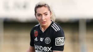Maddy Cusack portant le maillot noir de Sheffield United avec l'emblème du coquelicot, concentrée sur le terrain pendant un match, faisant preuve de détermination.